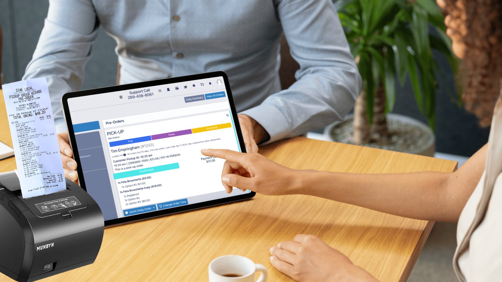 A user reviews the simple structure of an online order from Dine Local on a tablet, while a printer with a printed order chit sits beside showing the simple structure of a large order.